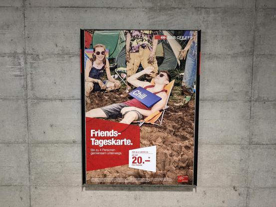 Freundes-Tageskarte-Werbung der SBB auf Sichtbetonwand. Darauf Jugendliche beim Chillen auf Liegestühlen im Matsch, mutmasslich an einem Open-Air-Festival.

Auf dem Bauch hat ein Jugendlicher ein Bahnhofsschild «Chill»