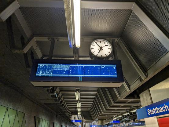 Bild eines Bahnhofs mit einer blau-weissen Abfahrtsanzeige, welche zufällige Pixelmuster anzeigt