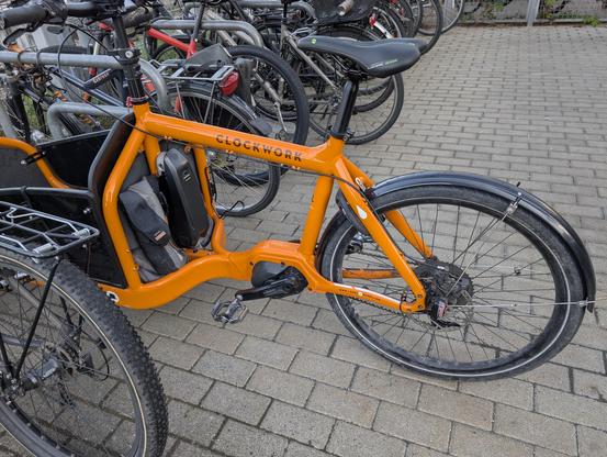 Ein oranges Lastenrad der Marke Clockwork neben anderen abgestellten Velos