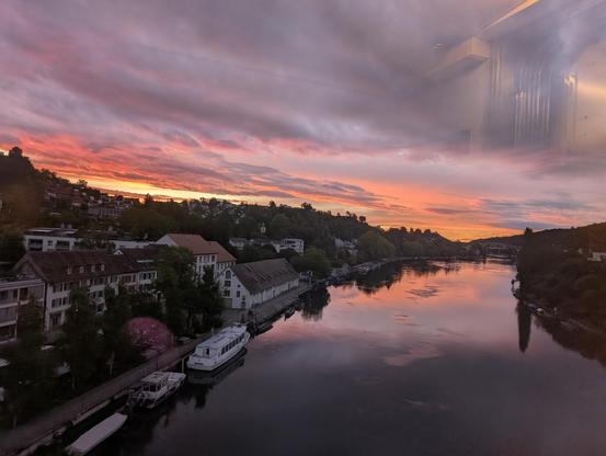 Blick ab einer Brücke einem Fluss entlang; der Horizont ist blutrot