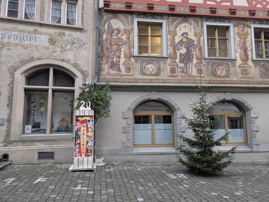 Blick auf eine Stele mit Märchenfiguren und der Aufschrift "Märliweg". Diese steht vor jahrhundertealten, bemalten Gebäuden, für die Stein am Rhein berühmt ist.