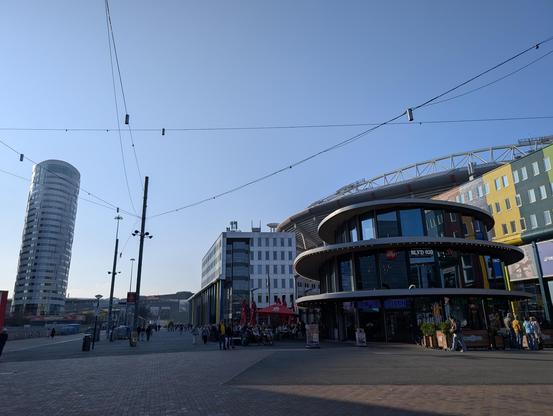A plaza with some buildings to the right. On the left hand side, there is a round (office) tower, looking like it is tilted