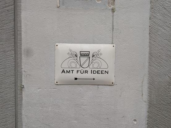 Halbwegs offiziell aussehendes Schild "Amt für Ideen" mit Pfeil in Richtung einer Tür