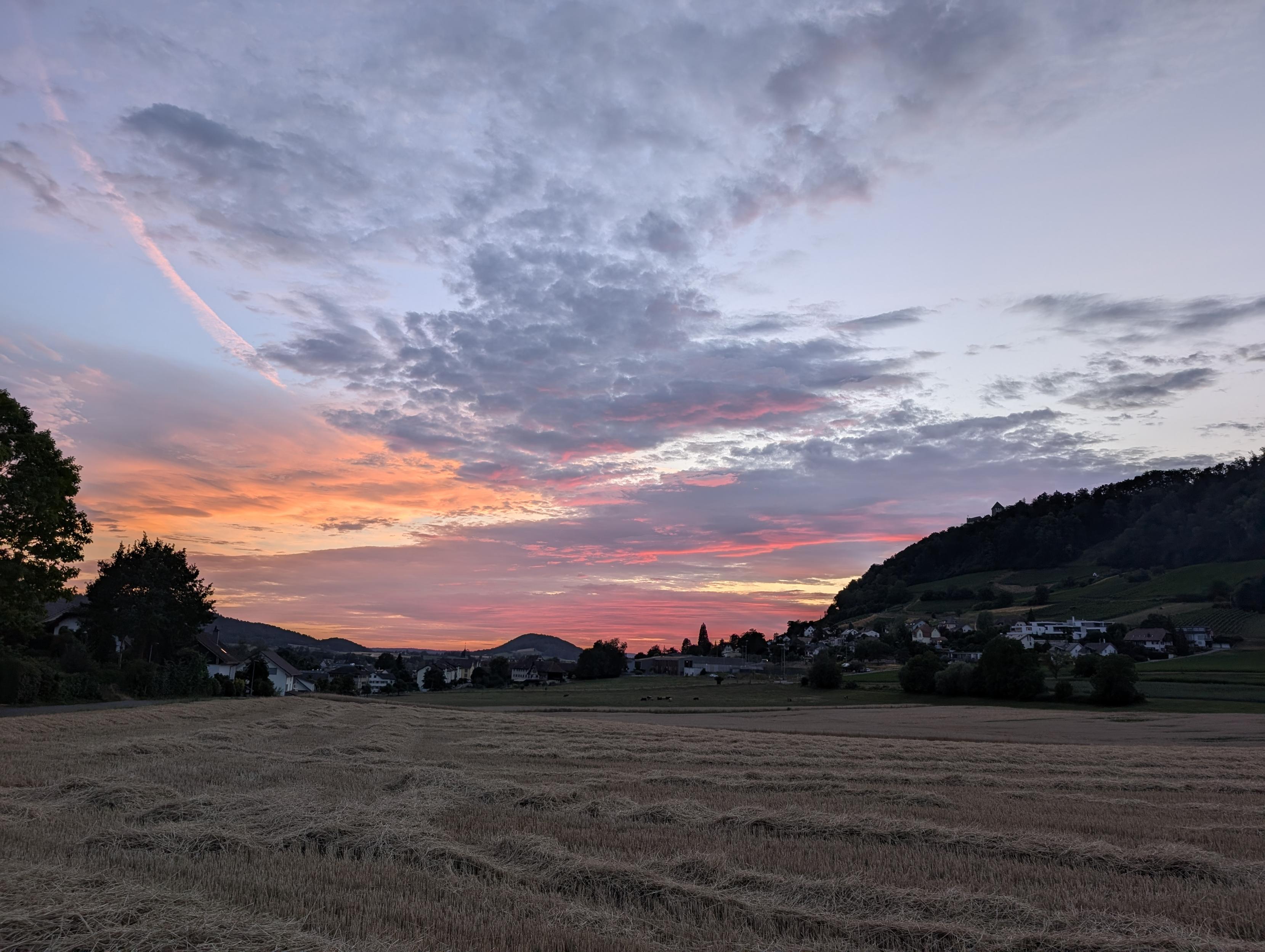Blick über ein abgeerntetes Feld auf einen roten Sonnenuntergang