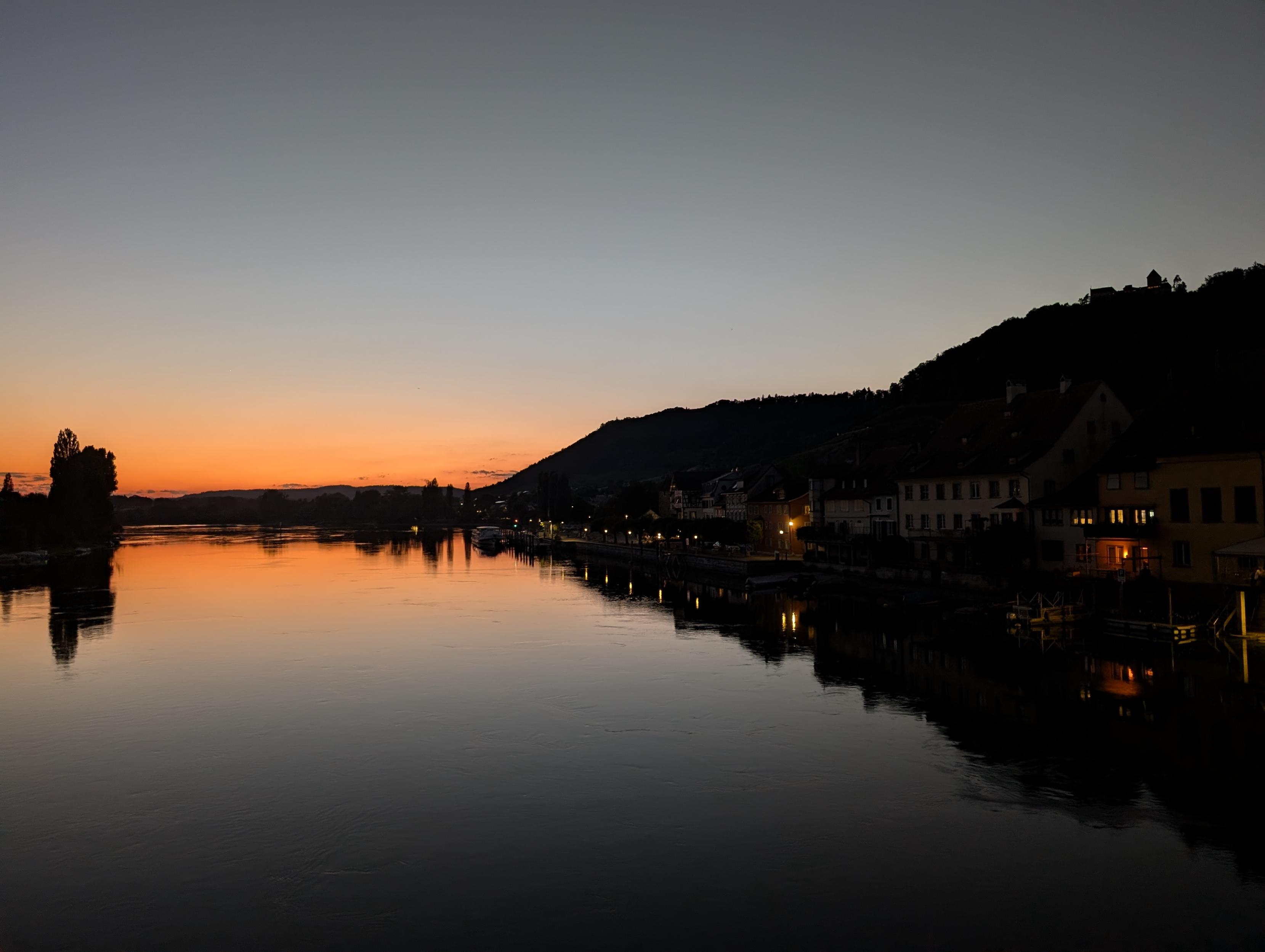 Leuchtendes Abendrot spiegelt sich in einem Fluss neben einem schwar sich abzeichnenden Hügelzug