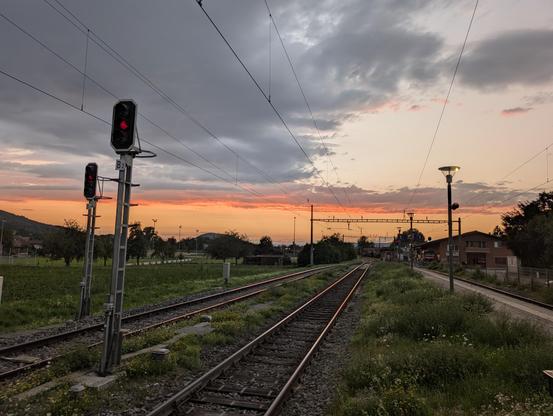 Ein breiter roter Sonnenuntergang, aufgenommen ab einen Bahnhof mit einigen sichtbaren roten Ampeln