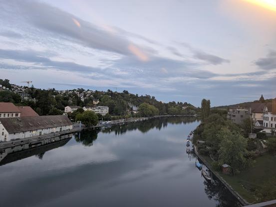 Blick ab einer Brücke über einen Fluss, links und rechts von kleinstädtischen Gebäuden und Bäumen bestanden